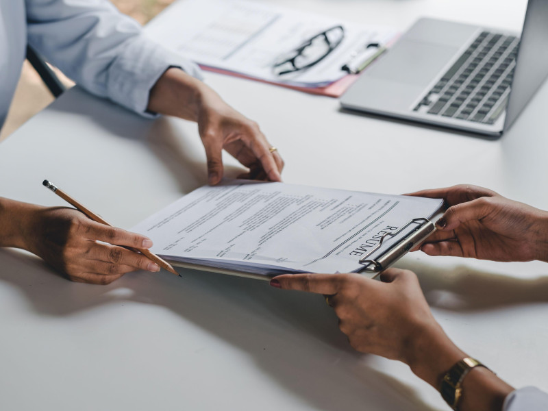 Mujer de negocios sosteniendo su currículum y hablando con una candidata durante una reunión corporativa o una entrevista de trabajo: concepto de negocios, carrera y colocación