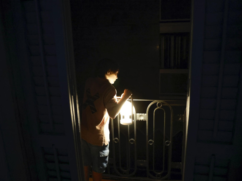 Un niño con una lampara mira desde el balcón la calle todavía a oscuras esta madrugada